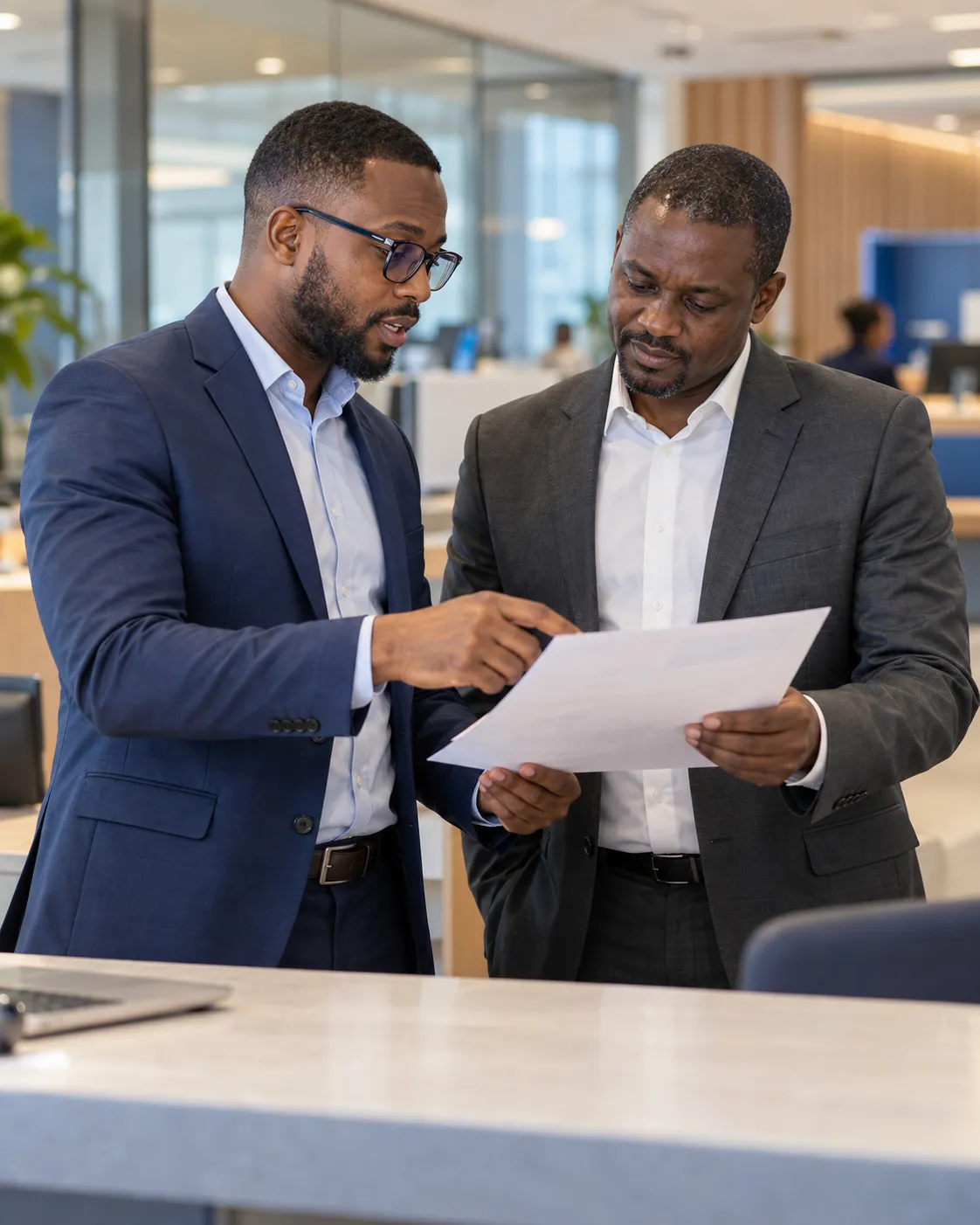 Two bank managers in suits reviewing a report together in an open-plan office